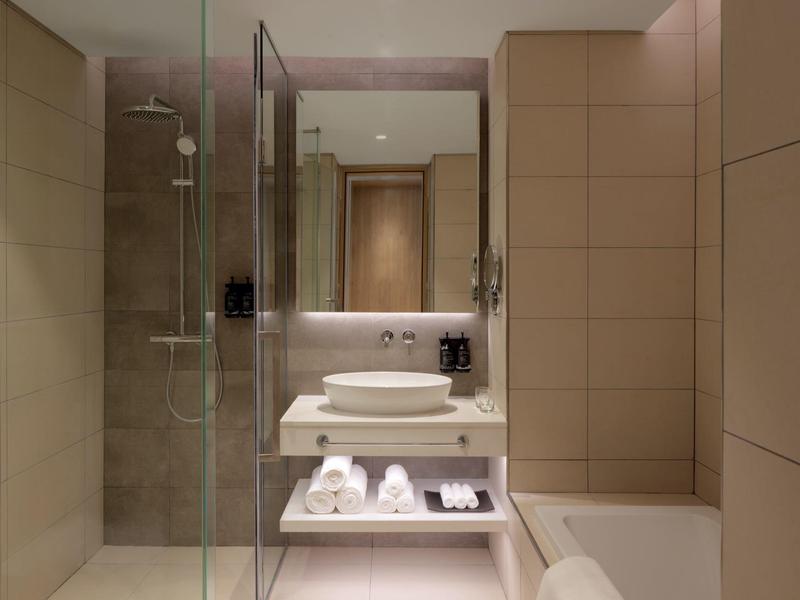 Modernes Badezimmer mit hellen Fliesen, Glasdusche, Waschbecken und indirekter Beleuchtung.