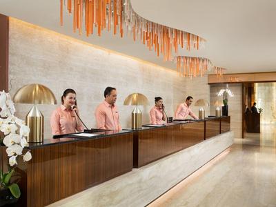 Hotelová recepce se čtyřmi zaměstnanci v jednotných uniformách za dlouhým pultem.