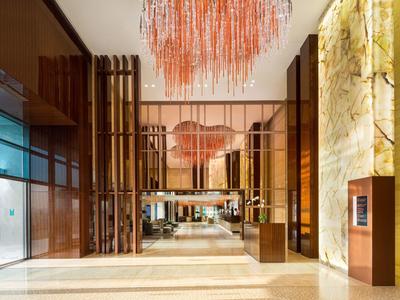 Luxusní hotelová hala s moderními dřevěnými panely a velkým červeným lustrem.