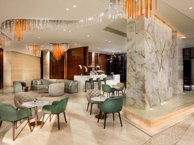 Elegantní hotelová lobby s zelenými křesly, kulatými stoly a stylovým osvětlením.