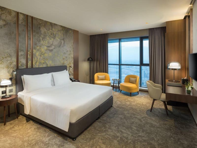 Moderní hotelový pokoj s velkou postelí, dvěma křesly a výhledem na město.