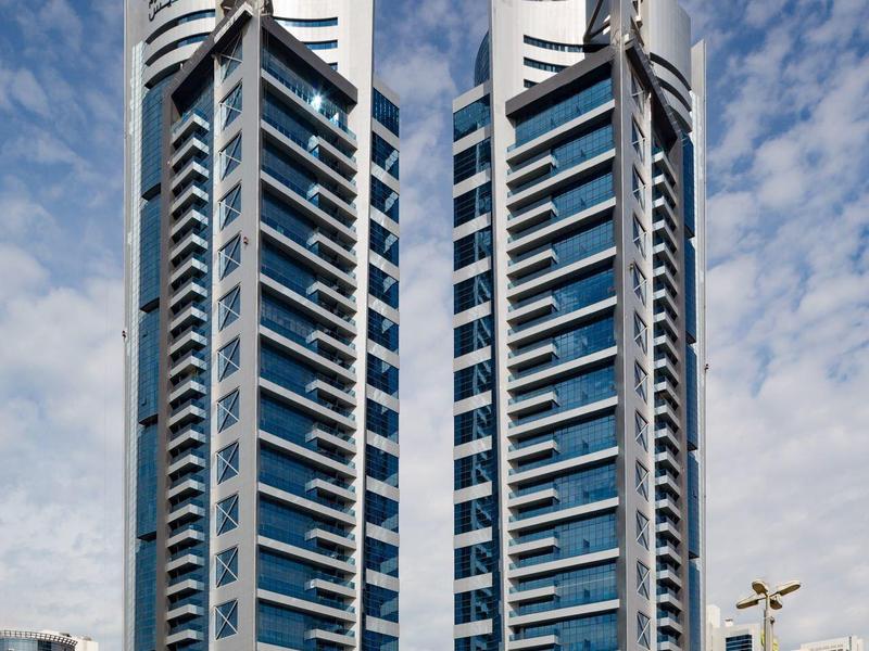 Vysoký moderní hotel se dvěma věžemi a výraznými špičkami na střeše pod oblačnou oblohou.