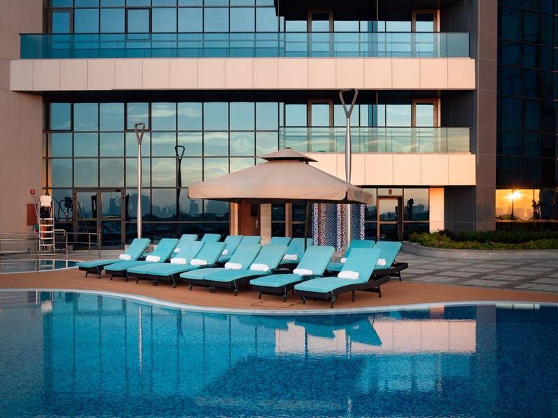 Moderní hotel s venkovním bazénem, lehátky a slunečníkem před skleněnou fasádou