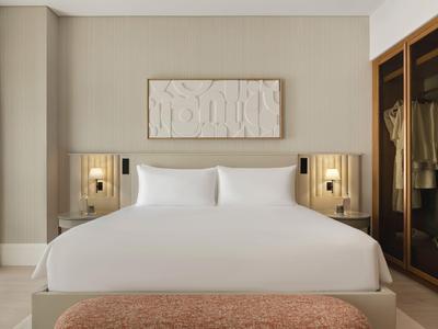 Jasny pokój hotelowy z dużym łóżkiem podwójnym, minimalistyczną dekoracją i garderobą.