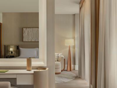 Nowoczesny pokój hotelowy z biurkiem, krzesłem i widokiem na sypialnię z lampą stojącą.