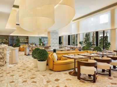 Helles Hotelrestaurant mit modernen Möbeln und großem, geschwungenem Deckenlicht.