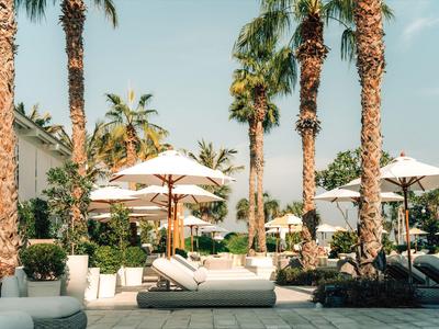 Poolbereich mit Liegen, Sonnenschirmen und Palmen bei klarem Himmel