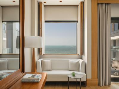 Jasny pokój hotelowy z widokiem na morze, białą sofą i małym stolikiem.