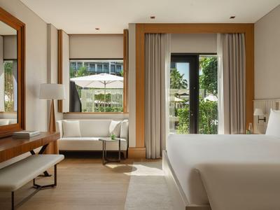 Jasny pokój hotelowy z dużym łóżkiem, sofą, biurkiem i widokiem na balkon.