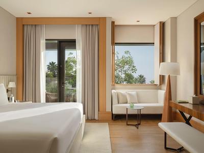 Helles Schlafzimmer mit weißem Bett, Sofa, Holzmöbeln und Fenster mit Blick ins Grüne.