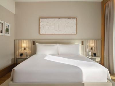 Modernes Schlafzimmer mit großem Bett, weißen Wänden, Holzdetails und lichtdurchflutetem Fenster.