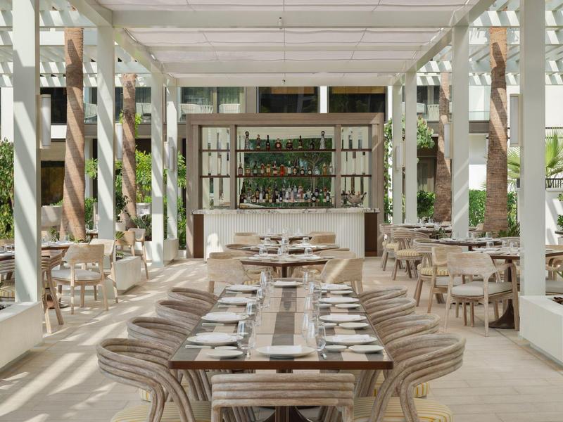 Jasny, nowoczesny teren zewnętrzny hotelu z stołami, krzesłami i barem.