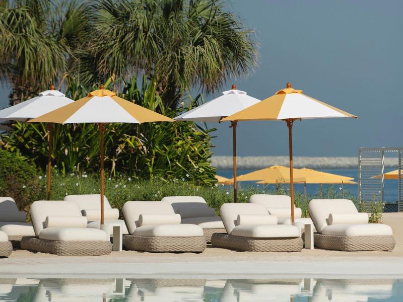 Basen z leżakami i parasolami przed palmami i morzem przy czystym niebie.