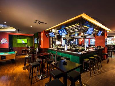 Moderne hotelbar met pooltafel, meerdere schermen en houten stoelen bij tafels en bar.