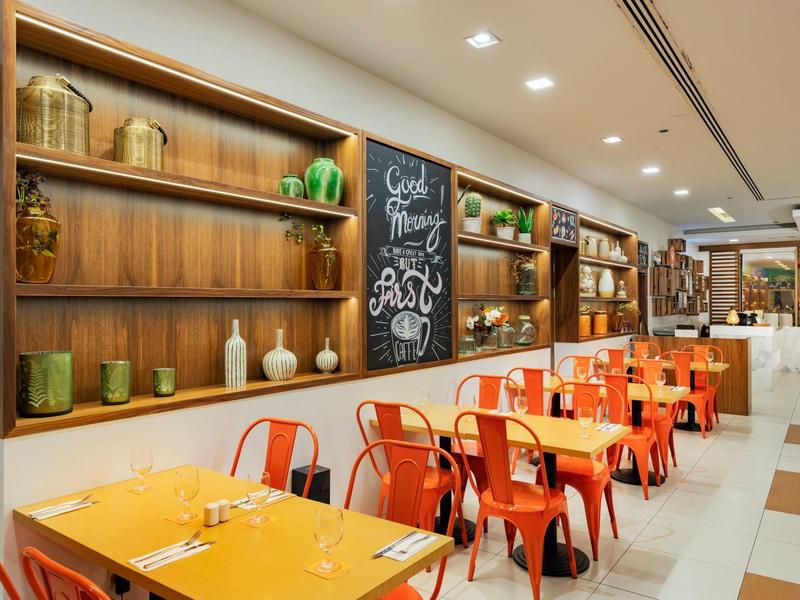 Modern restaurant met tafels, oranje stoelen en planken met decoraties aan de muur.