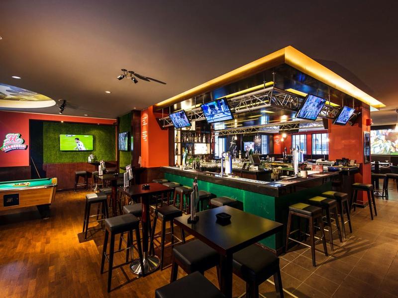 Moderne hotelbar met pooltafel, meerdere schermen en houten stoelen bij tafels en bar.