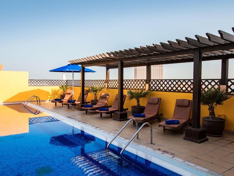 Zwembadgedeelte met ligstoelen en parasols onder een pergola bij een heldere lucht.