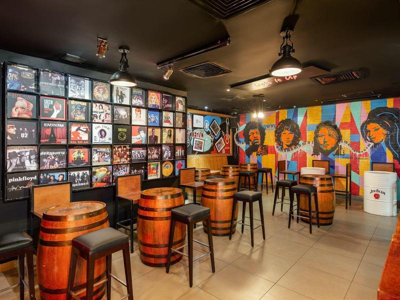 Rustieke bar met vattafels, houten krukken en kleurrijke muur met foto's en kunst