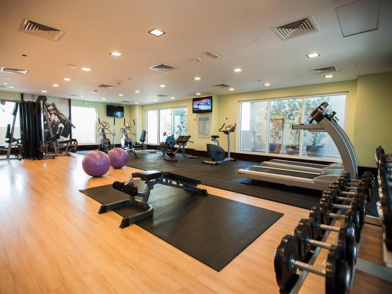 Ruime fitnessruimte met halters, trainingsapparatuur en fitnessballen op houten vloer.