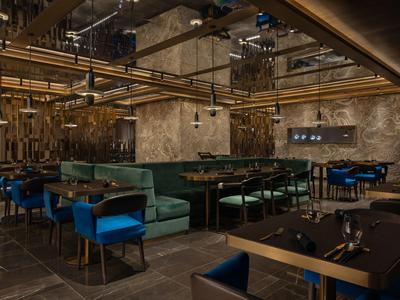 Restaurant moderne avec intérieur sombre, canapés verts et chaises bleues sous un éclairage doré.
