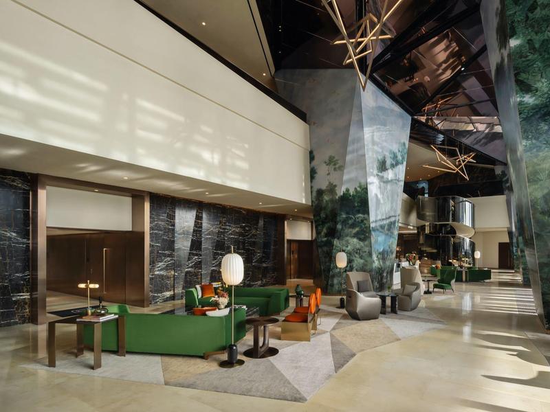 Hall d'hôtel moderne avec canapés verts, colonnes en marbre et plafond élevé.