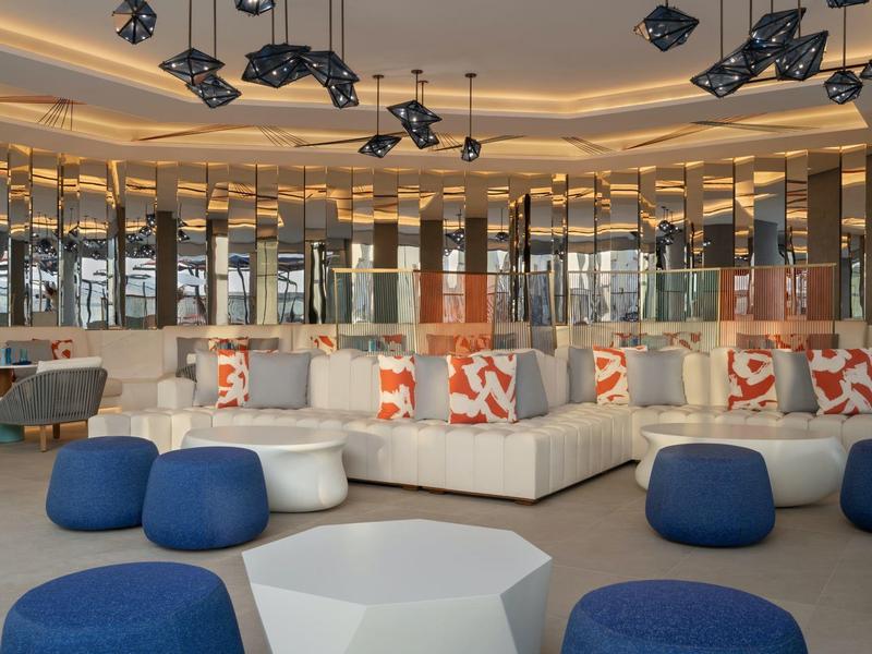 Hall d'hôtel moderne avec des coins salon confortables et des coussins décoratifs sous un éclairage chaleureux.