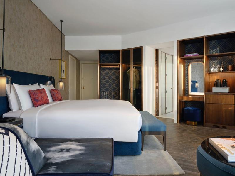 Chambre d'hôtel moderne avec grand lit, coin salon et garde-robe ouverte avec éclairage.