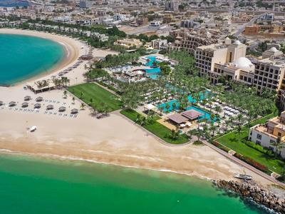 Luftaufnahme eines Resorts am Strand mit Pools und grüner Landschaft am Meer.