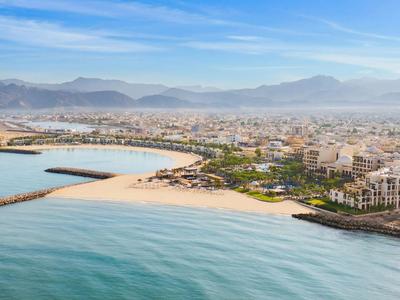 Miasto nadmorskie z plażą, morzem i górami w tle pod bezchmurnym niebem.