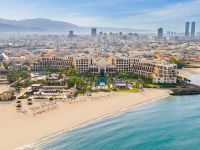 Widok z lotu ptaka na ośrodek wypoczynkowy na piaszczystej plaży obok miasta z górami w tle.