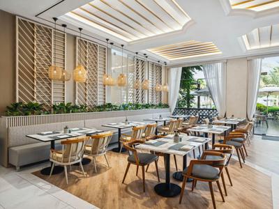 Nowoczesna restauracja hotelowa z drewnianą podłogą, wygodnymi krzesłami i dużymi oknami wpuszczającymi światło dzienne.