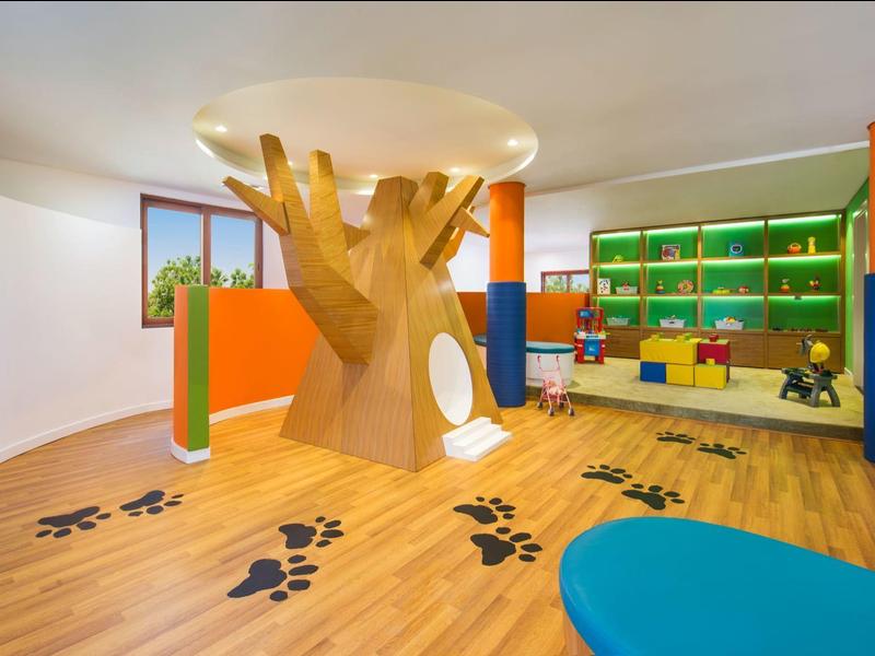 Kinderspielzimmer mit großem Baumhaus, bunten Säulen und schwarzen Fußabdruckbodenaufklebern.