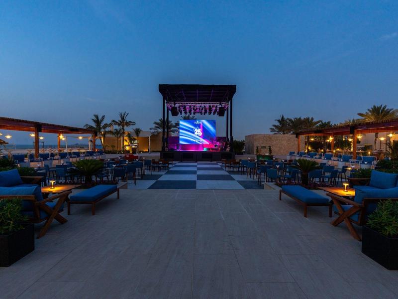 Outdoor-Kinobereich in einem Hotel mit Lounge-Sitzplätzen und LED-Bildschirm bei Dämmerung.