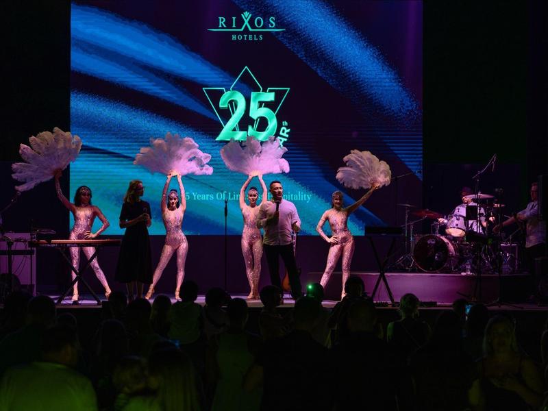 Bühnenperformance mit fünf Tänzern, leuchtender 25-Jahreszahl, dunkler Hintergrund, Publikum im Vordergrund.