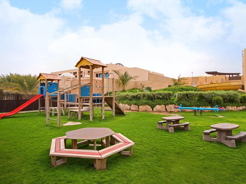 Paar geht am Sandstrand entlang, blauer Himmel, ruhiges Meer, Palmen am Horizont.