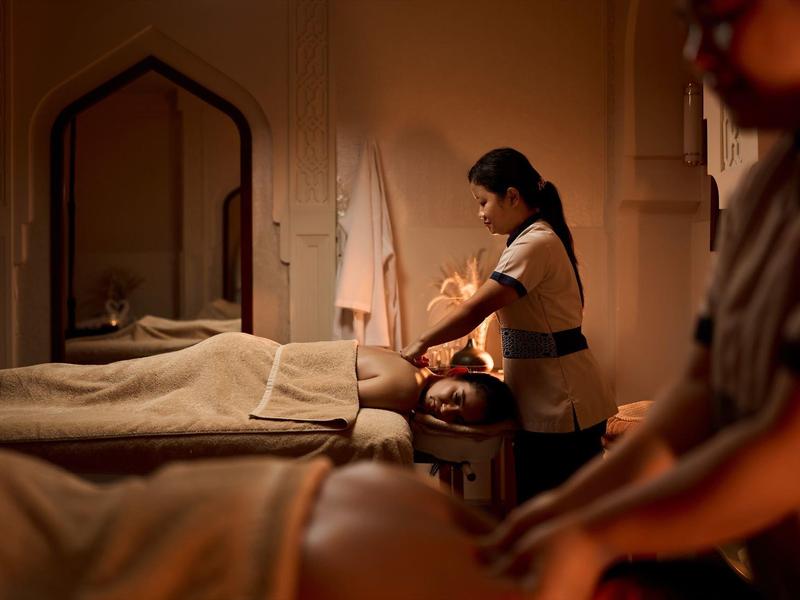 Ruhiger Massageraum mit warmem Licht, zwei Personen erhalten entspannende Rückenmassagen.