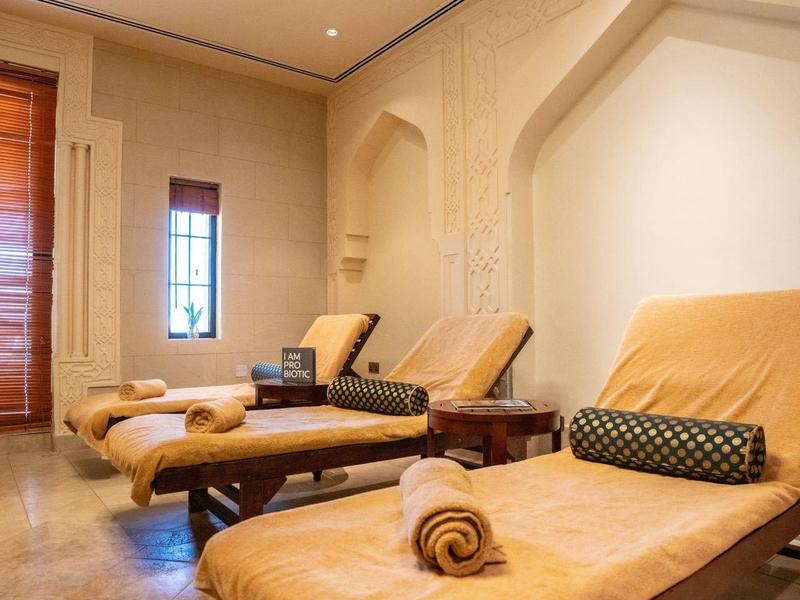 Hell beleuchteter Raum mit drei braunen Liegen, Handtüchern und weichen Kissen an der Wand.