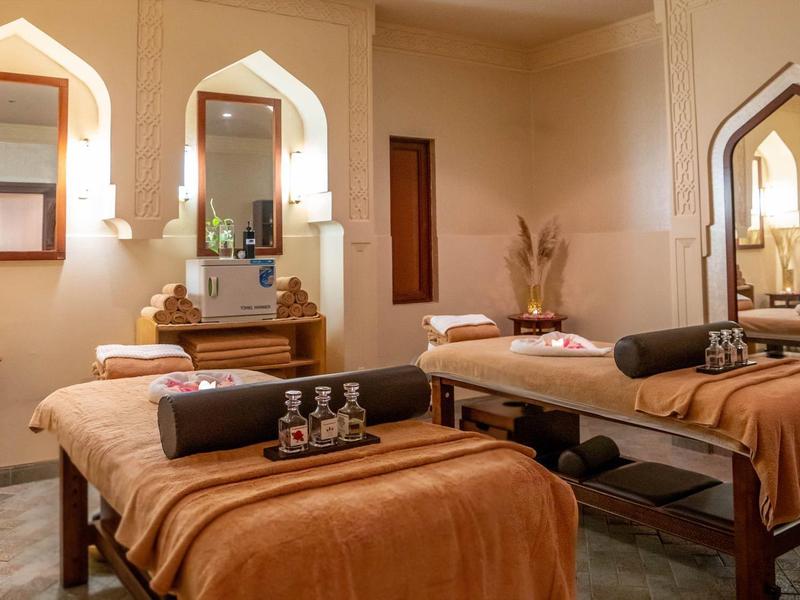 Zwei Massageliegen mit braunen Decken und Kissen in gemütlichem, warm beleuchtetem Spa-Raum.