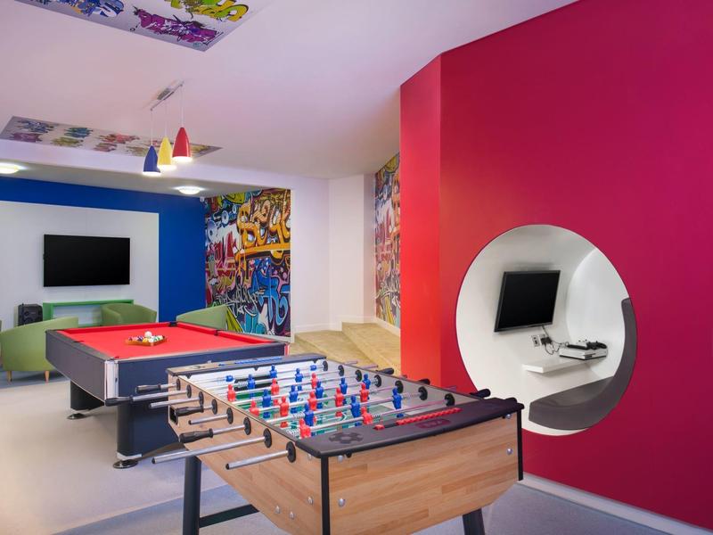 Modernes Spielzimmer mit Tischtennis, Kicker, Billardtisch und buntem Wanddesign.