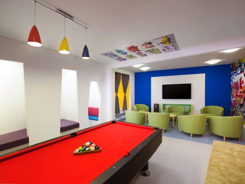 Moderner Freizeitraum mit rotem Billardtisch, bunten Hockern und Sofa vor Fernseher.