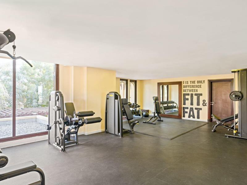 Großer Fitnessraum mit modernen Geräten, Spiegeln an der Wand und Fensterfront für viel Tageslicht.