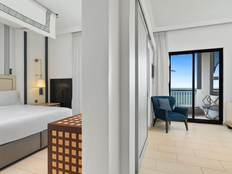 Modern eingerichtetes Hotelzimmer mit Doppelbett, Balkon und Meerblick. Helle Farben und klare Linien.