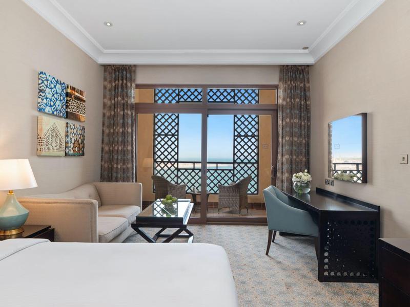 Helles Schlafzimmer mit großem Fenster, Bett, Sofa, Schreibtisch und dekorativen Wänden.