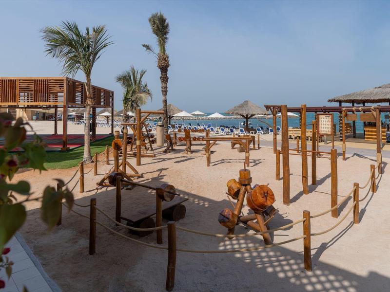 Strand mit Holzkonstruktionen, Sand, Palmen und Blick auf das blaue Meer unter klarem Himmel.
