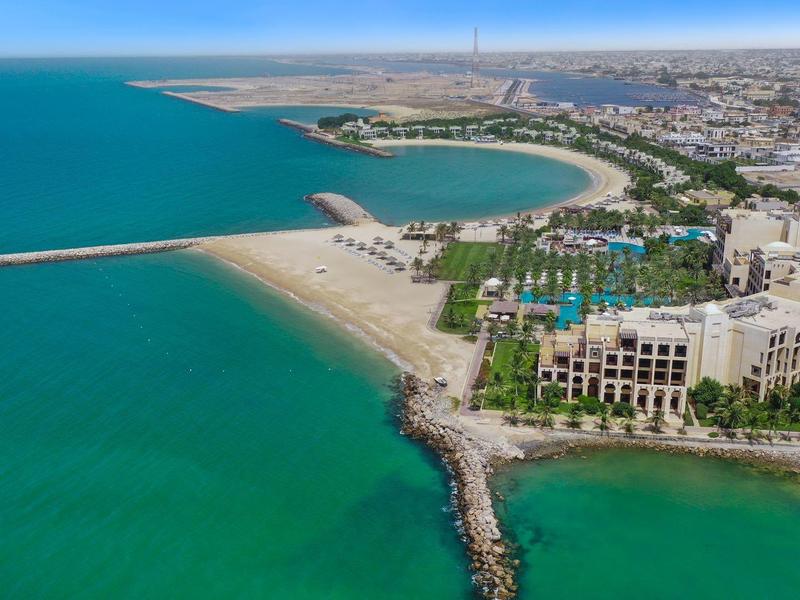 Küste mit Sandstränden, türkisblauem Wasser und Gebäuden entlang der Uferpromenade bei sonnigem Himmel.