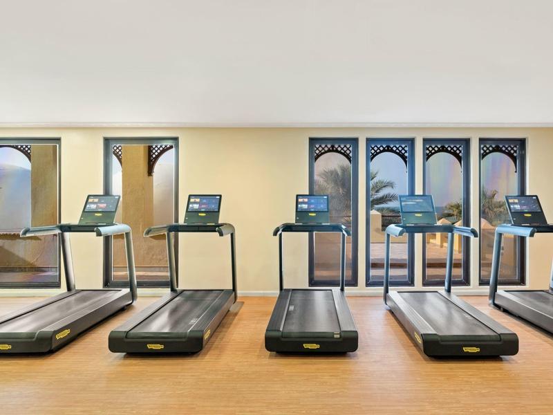 Helles Fitnessstudio mit fünf modernen Laufbändern vor großen Fenstern und Holzboden.