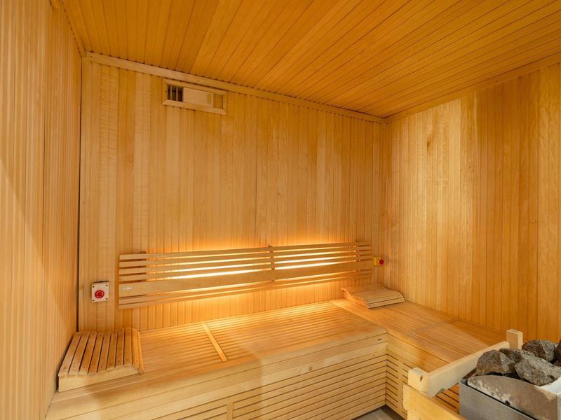 Helle Holzsauna mit Sitzen, Rückenlehne, Steinen und sanfter Beleuchtung im Raum.