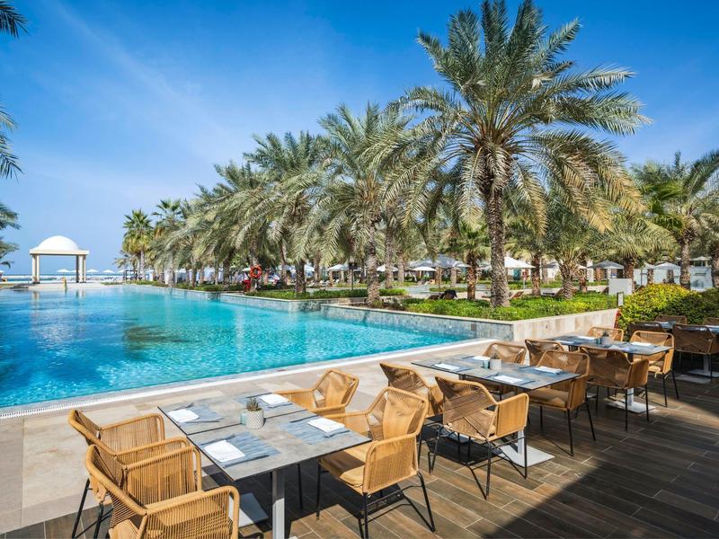 Restaurantterrasse mit Blick auf einen Pool und Palmen unter blauem Himmel
