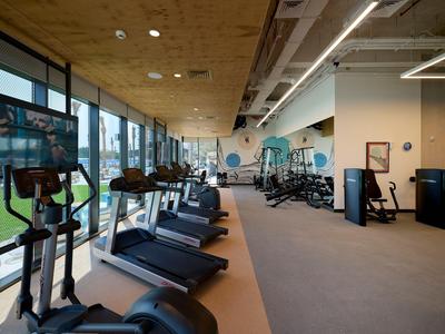 Moderner Fitnessraum mit Laufbändern und Fitnessgeräten neben großen Fenstern.