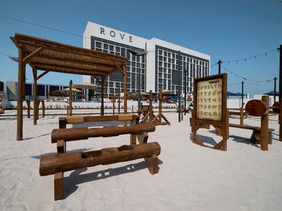 Strandspielplatz mit Holzgeräten vor einem Hotelgebäude am Sandstrand.